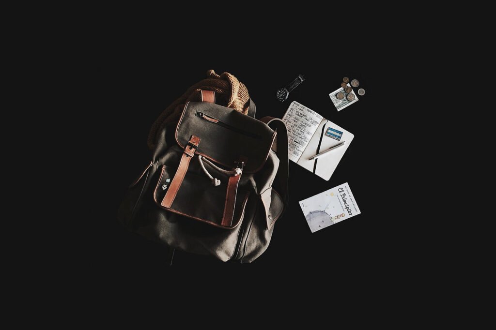 Backpack, notebook, pens, watch and coins on a dark background.